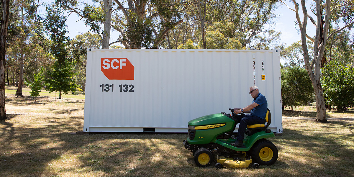 A jolly old fellow riding a mower with a 20ft SCF shipping container in the background